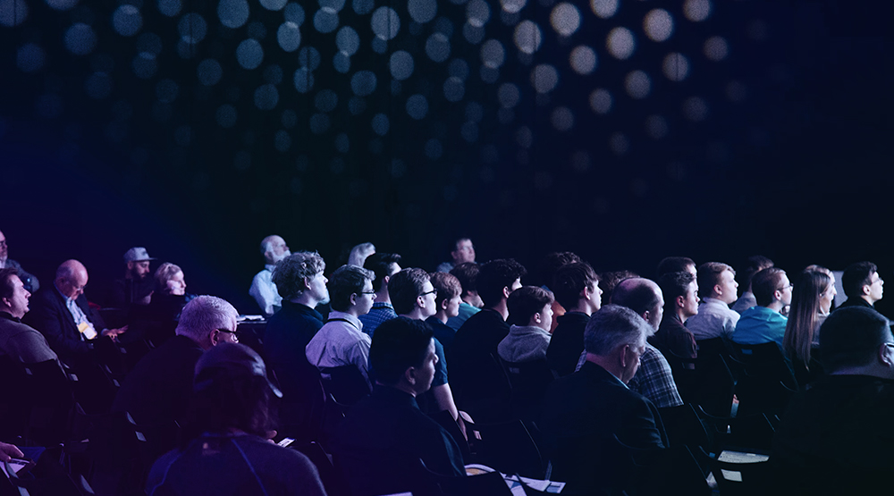 Audience in dark room staring off camera towards stage