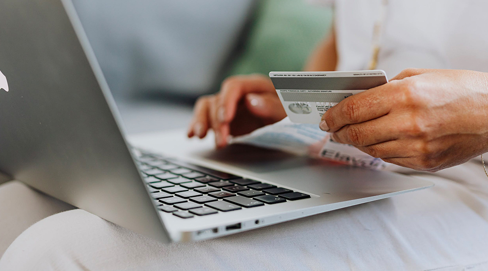 Hands shown at laptop with person holding credit card