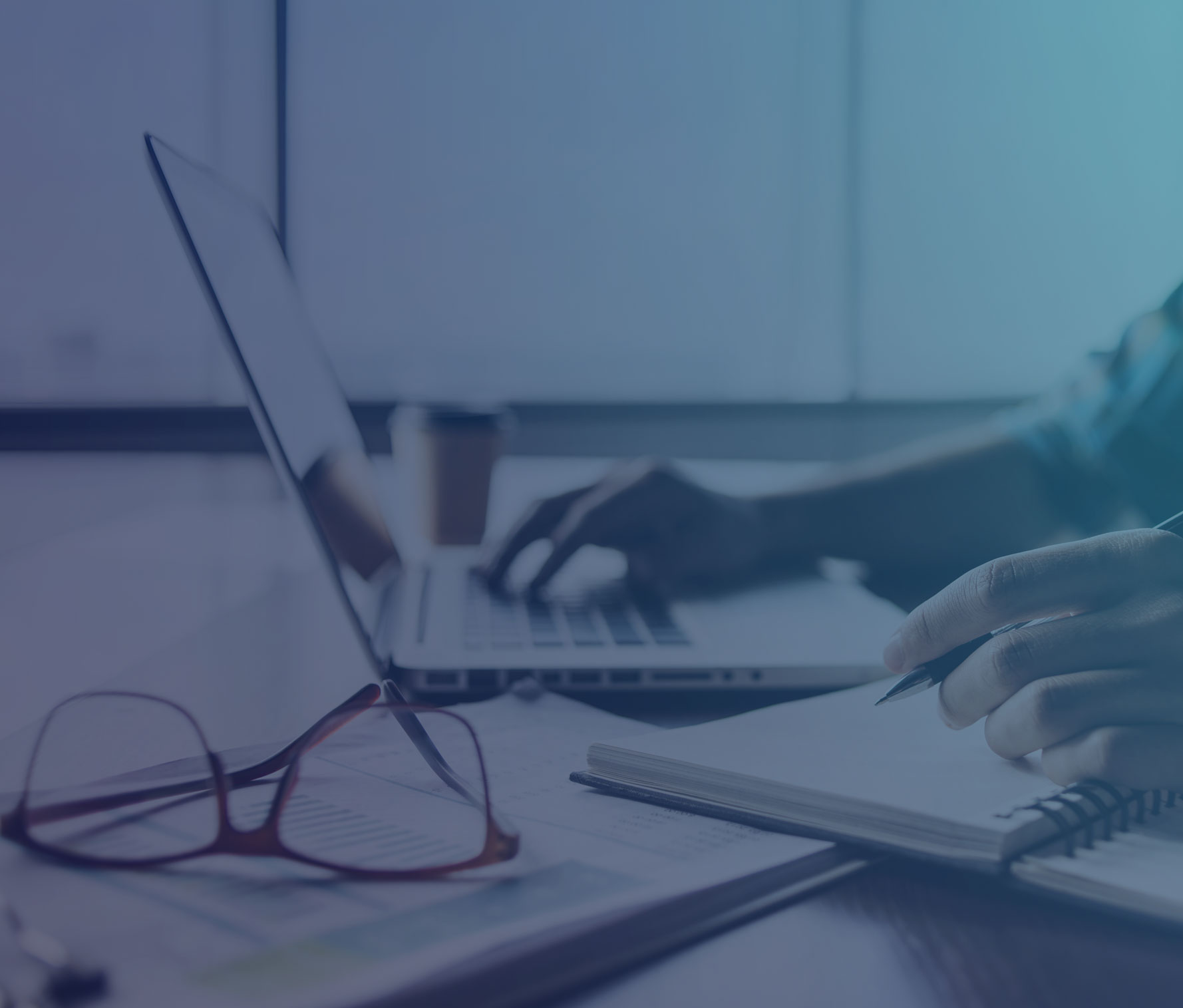 Man typing on a computer and writing on a notepad at a desk