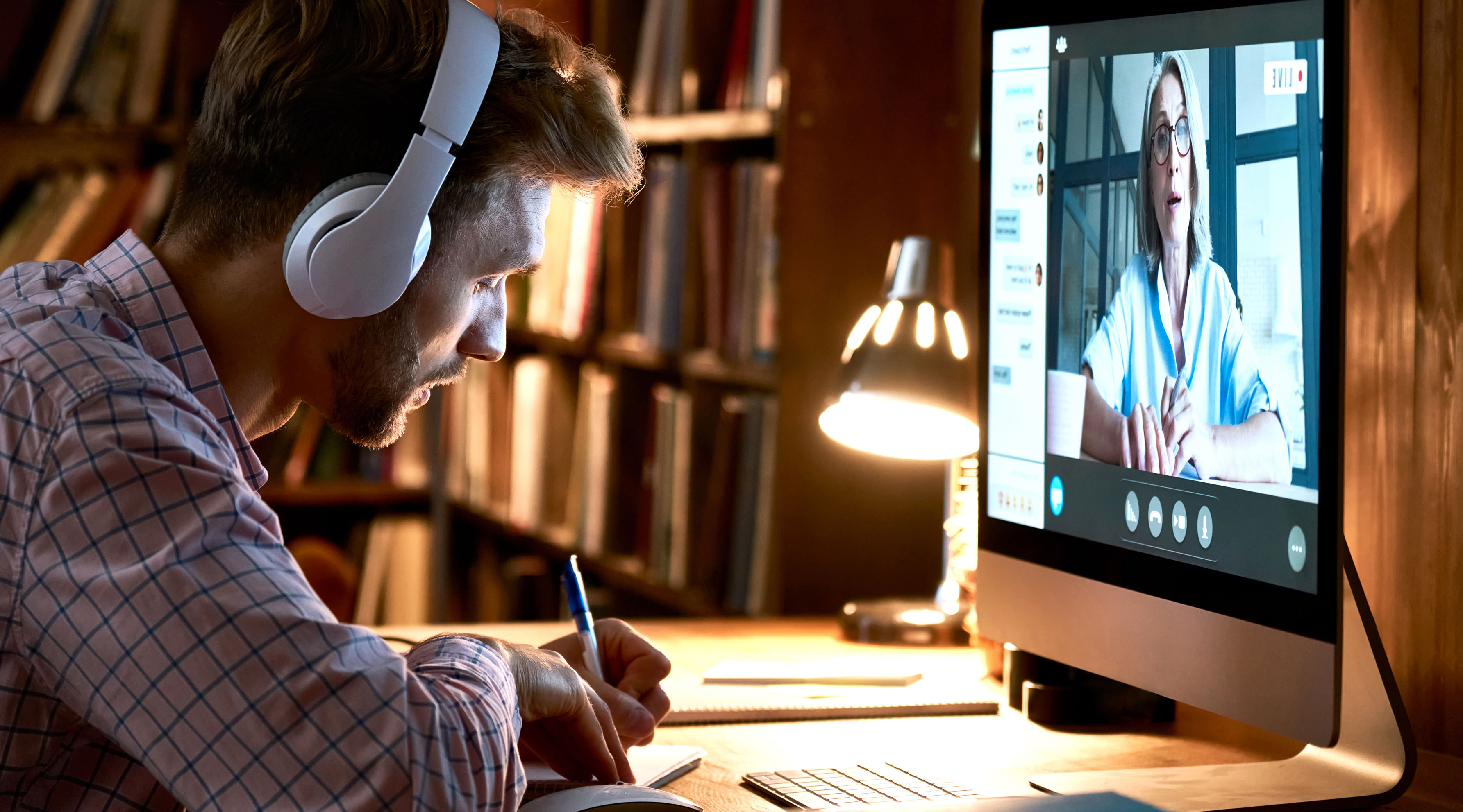 Man wearing headphones taking notes and watching a live virtual class