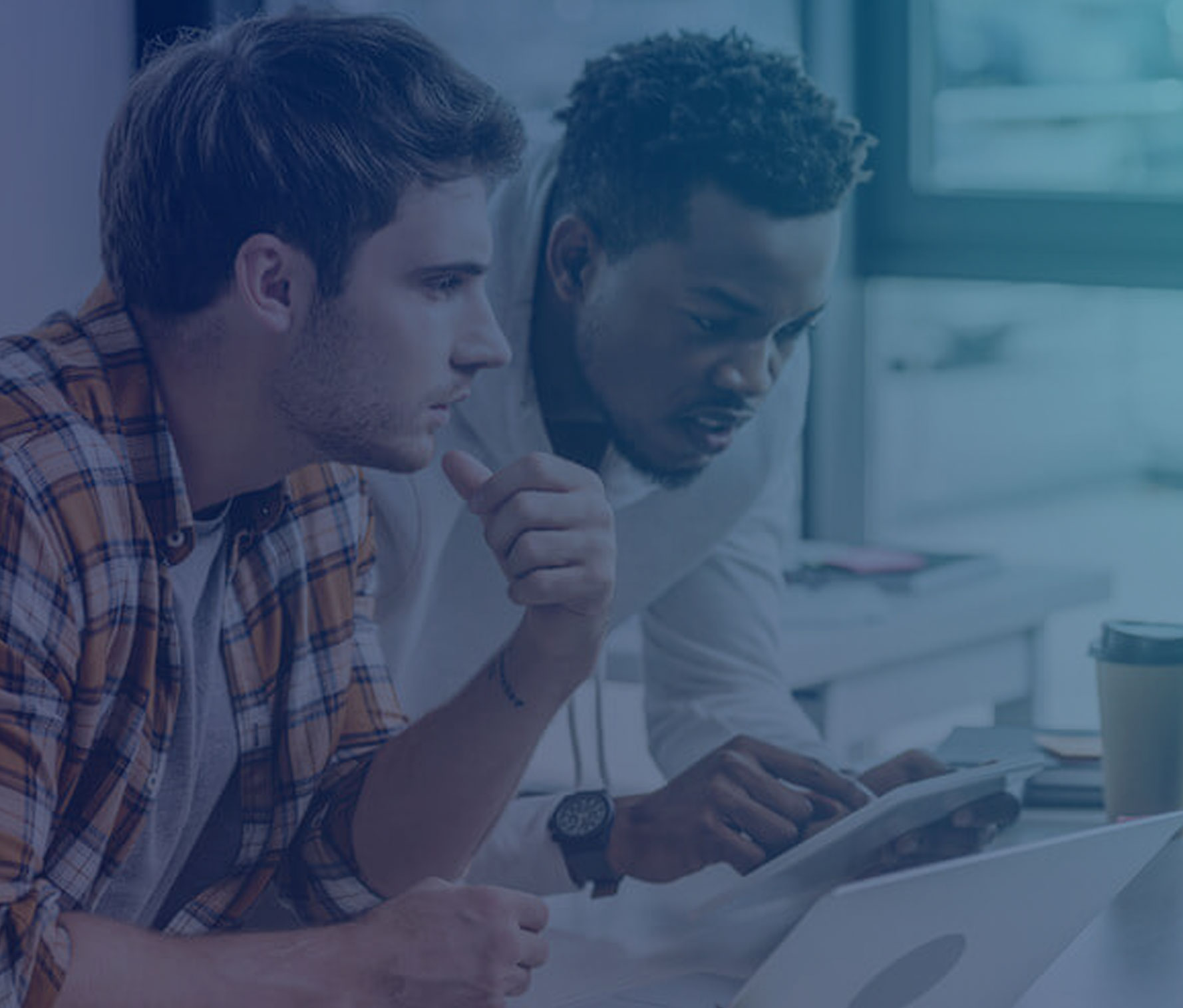Two staff members are using computers and tablets at a desk.
