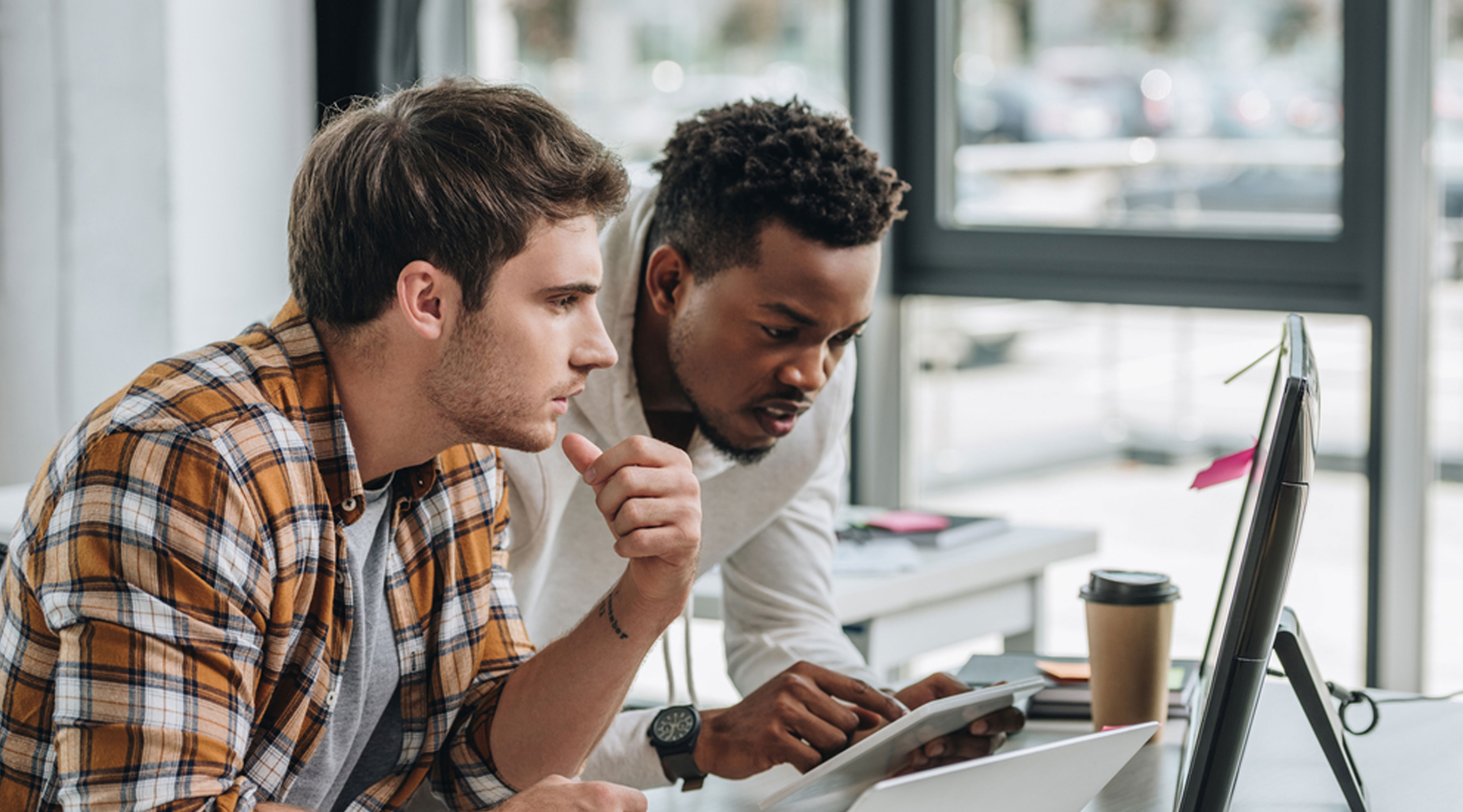 Two staff members are using computers and tablets at a desk.