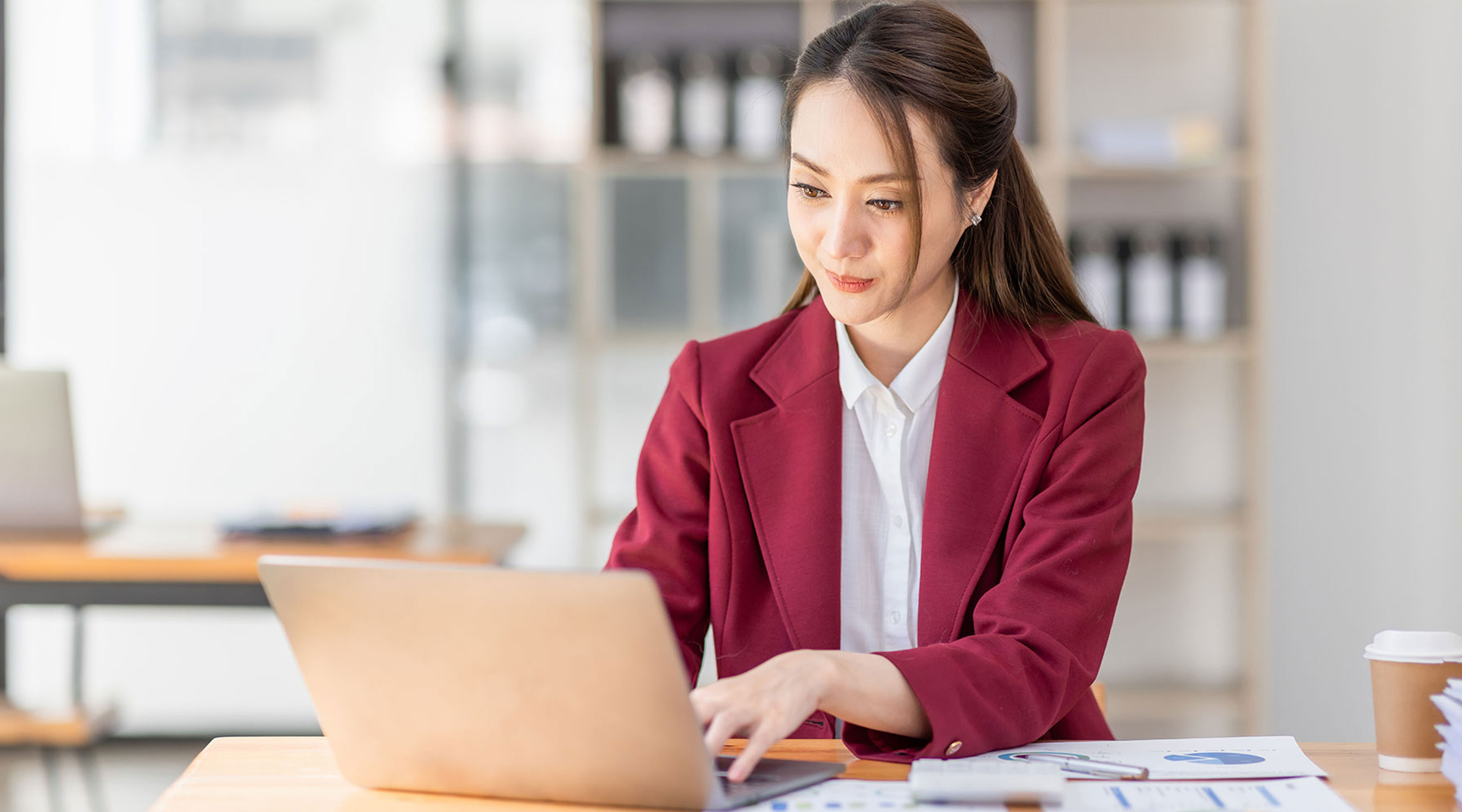 This image shows a woman sitting at her desk typing on a laptop. 