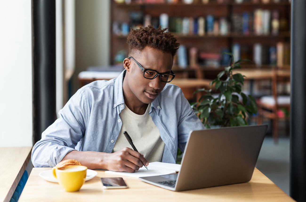 Person looking at a laptop and writing on a piece of paper